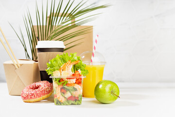 Fitness food set of coffee, orange juice, shrimp salad, noodles in box, donut, apple, packet in white interior, palm leaf. Mockup advertising for delivery service, take away restaurant, online order.