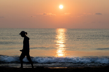 A girl, a teenager walks alone on the beach at sunrise. Loneliness, future plans - concept. Silhouette. 