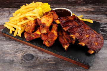 Barbecue pork ribs and chicken wings with French fries and sweetcorn on the cob