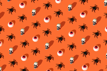 Fototapeta na wymiar Creative spooky pattern made of spider, skull and eye on orange background. Halloween concept.