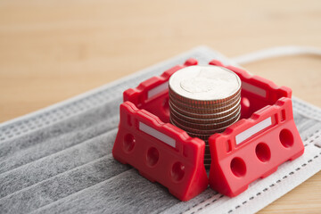Red under construction barrier around stacked coins on mask. World economy crisis due to COVID-19,...