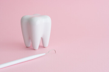 White healthy tooth model and dental pick explorer probe on pink background with copy space. Dental care and healthcare concept.