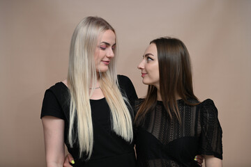 Portrait of two girls blonde and brunette look at each other with a smile