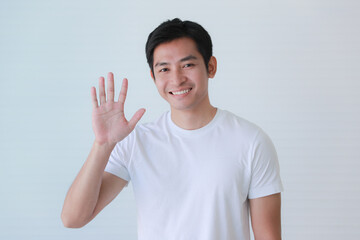 Studio portrait shot of Asian happy young handsome smart teenager teen guy model in casual clothing smiling show teeth look at camera waving hand greeting say hello hi of goodbye on white background - obrazy, fototapety, plakaty
