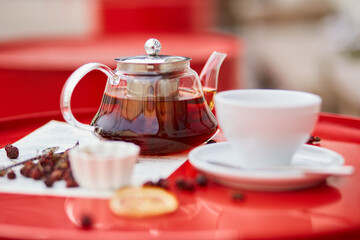Hot tea in glass teapot and cup, on red background