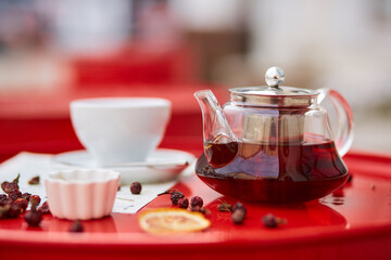 Hot tea in glass teapot and cup, on red background