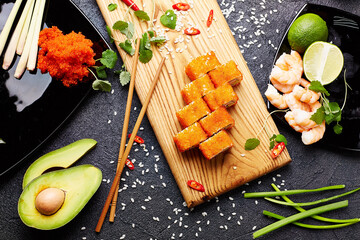 Set of various sushi rolls with soy sauce, srimps and chopsticks over dark background