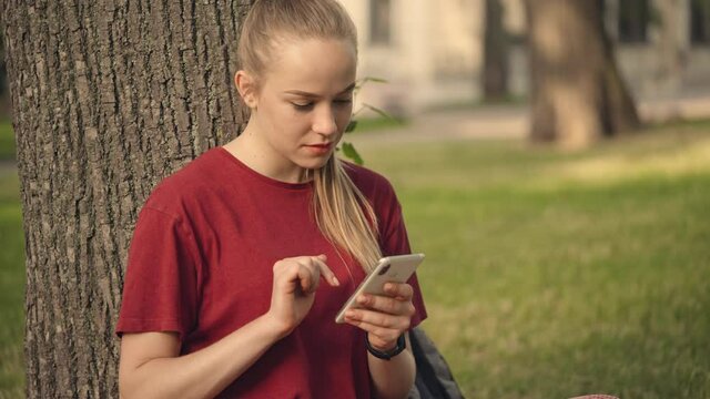 Young blond woman scrolling social media on smartphone, chatting with friends