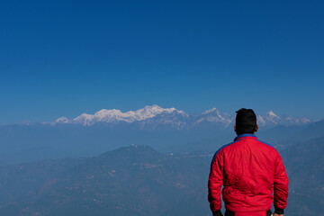 young Indian man standing looking at snowy mountains landscape.