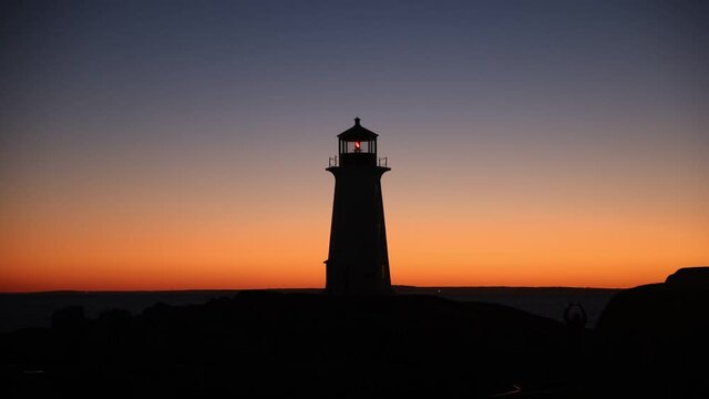 Silhouette shot of the famous Peggy's Cove Lighthouse during a dramatic sunset captured at the blue hour as the visitors take pictures.  Glow of sun on the far right.  Atlantic Coast, Nova Scotia