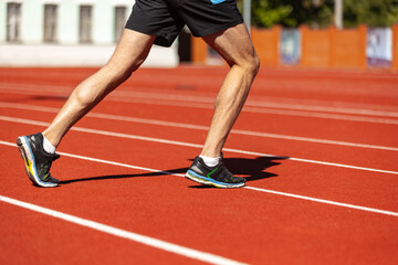 Fototapeta premium Cropped image of male athlete, runner training at public stadium, sport court or running track outdoors. Summer sport games. Man's legs