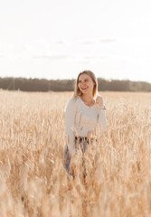 A young beautiful girl in a denim skirt walks through a wheat field on a sunny day