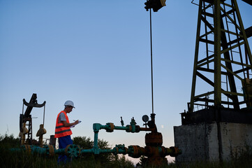 Side view of oil well worker who writing results of pipeline inspection on clipboard. Engineer...