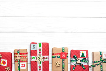 Fototapeta premium Handmade wrapped red, green gift boxes decorated with ribbons, snowflakes and numbers, Christmas decorations and decor on white table Xmas advent calendar concept Top view Flat lay Holiday card