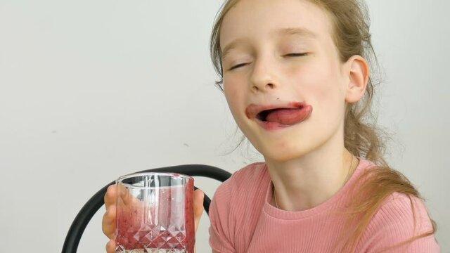 Sweet little girl drinks raspberry smoothie and smiles. Vegetarian drink. Close-up portrait of a child who enjoys a refreshing tasty raspberry juice, healthy eating