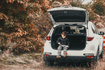 A child is sitting in the trunk of a car SUV or crossover with gouache paints, a car in the autumn forest