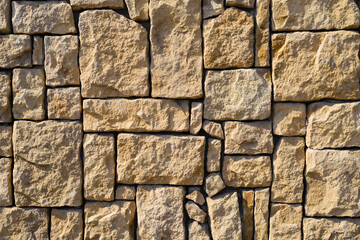 Rough yellow decorative stone of various sizes, imitation of old destroyed cobblestone. Texture brick wall background outdoor facade.
