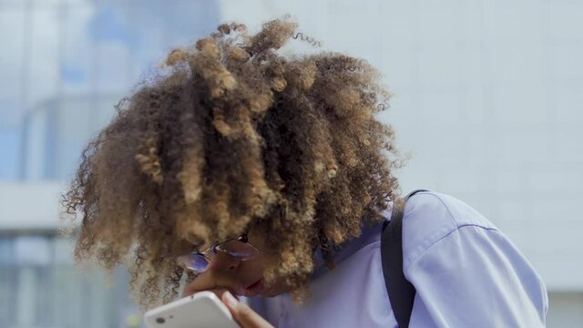 Faddish african american woman with curly hair holding smartphone and sneezing