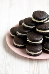 Homemade Oreos on a pink plate on a white wooden surface, side view.