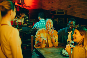 Obraz premium Happy friends having fun while drinking beer and talking to waitress in a bar.