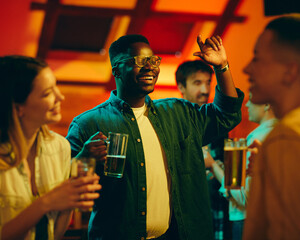 Young happy black man drinking beer and having fun with his friends in a bar.