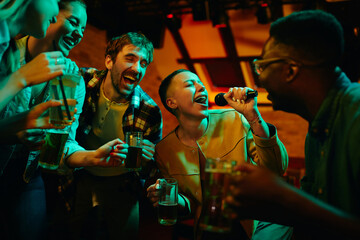 Cheerful friends having fun while singing karaoke during their night out in a pub. - obrazy, fototapety, plakaty