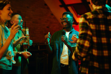Happy black man singing karaoke during the night out with his friends in a pub.