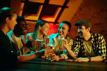 Young happy friends toasting with beer while gathering in a pub at night.