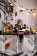 a little blonde girl is sitting at the kitchen table with vegetables and fruits and cooking