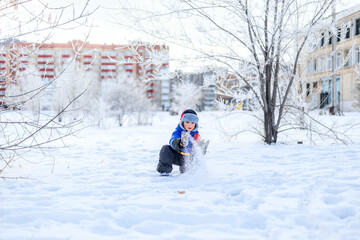 Fototapeta na wymiar Little boy having fun playing with fresh snow. Snow fight. Kid dressed in a warm clothes, hat, hand gloves.. Active outdoors leisure for child on nature in snowy winter day.