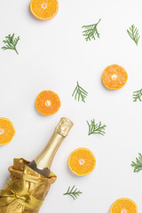 A bottle of champagne or wine in a beautiful golden package on a bright snow-white winter background with evergreen spruce leaves, thuja and juicy orange oranges, tangerines. Minimalistic new year hol