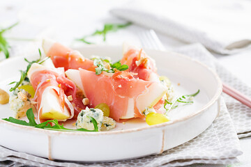 Appetizer with pear, blue cheese and prosciutto ham for holidays on a white plate.