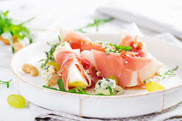 Appetizer with pear, blue cheese and prosciutto ham for holidays on a white plate.