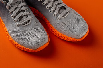 Pair of grooved orange sole sneakers from gray mesh fabric over orange background. Laced up stylish...