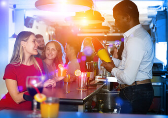 Portrait of man bartender shaking cocktail mixer for women in nightclub
