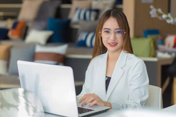 Fototapeta premium Asian professional business woman wearing glasses works at co-working space with laptop paper work (Business woman concept).