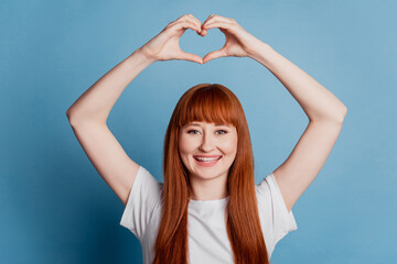 Cute girl making heart with fingers and smiling on blue background