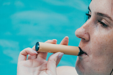 Woman smoking with electronic cigarette. Young woman smoking electronic cigarette in outdoors pool