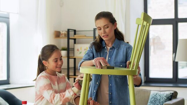 furniture renovation, diy and home improvement concept - happy smiling mother and daughter sanding old round wooden chair with sponge at home
