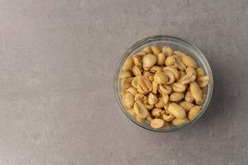 Salted peanuts flat lay in a glass bowl on a textured grey background with copy space