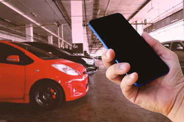 Hand holding smart phone device on blurred car parking background