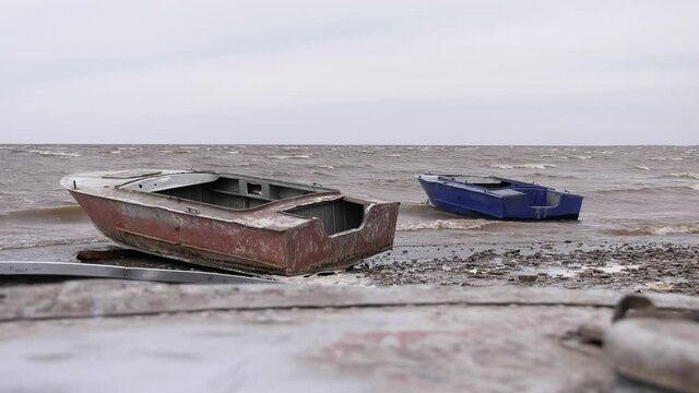 Two metal boats swaying on the waves near the shore. Windy autumn weather on the shore of Lake Ilmen.