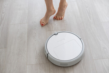 Human leg using smart robotic technology vacuum cleaner cleaning floor tiles background. Closeup...