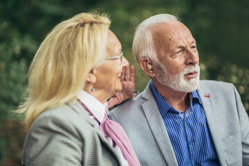 Senior couple with a hearing problem sitting on bench outdoor