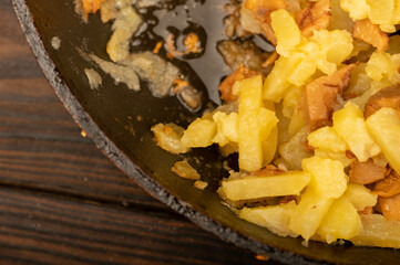 Potatoes fried in a frying pan with mushrooms on a wooden table. A traditional village dish.
