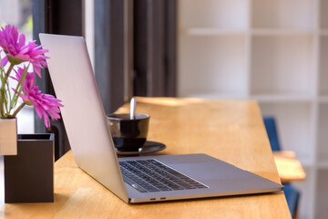 Laptop computer on wooden table with coffee cup and flower.