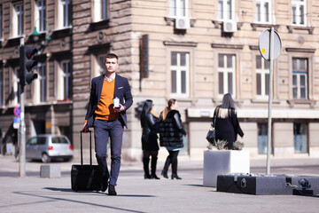 Businessman traveling with trolley luggage using smarthphone and drinking coffee..