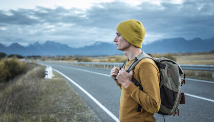 Man with a backpack on a road, against the background of mountains. Concept of freedom, autumn, travel and hiking
