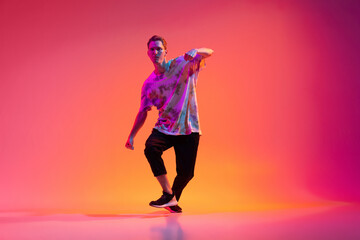 One energetic young man hip-hop dancer training isolated over gradient pink background in neon light