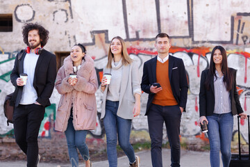 Group of people walking on a street with confidence. Businessmen and businesswomen traveling together. Old wall with abstract unrecognizable graffiti in the background..